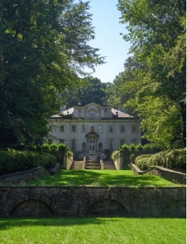 Grand estate surrounded by trees with a long stone staircase leading up to the mansion.
