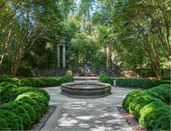 Peaceful garden courtyard with a circular fountain, manicured hedges, and stone pathways.