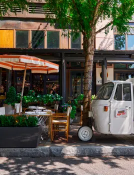 Pedestrian-friendly shopping plaza with outdoor dining areas, boutiques, and people walking under a glass canopy.