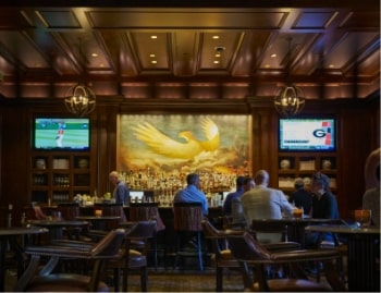 Upscale bar with wooden interiors, patrons seated at the counter, and a large mural of a golden phoenix behind the bar.
